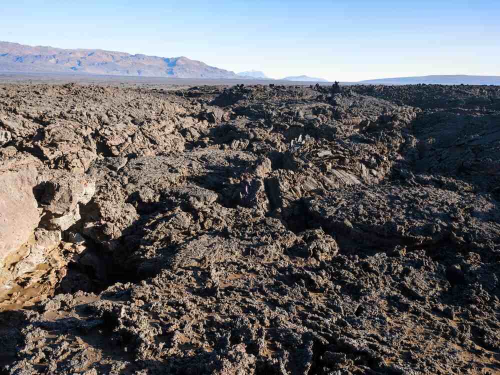 Étendue de lave noire et rugueuse à Holuhraun, formant un paysage volcanique aride sous un ciel dégagé, symbole des forces telluriques de l'Islande.