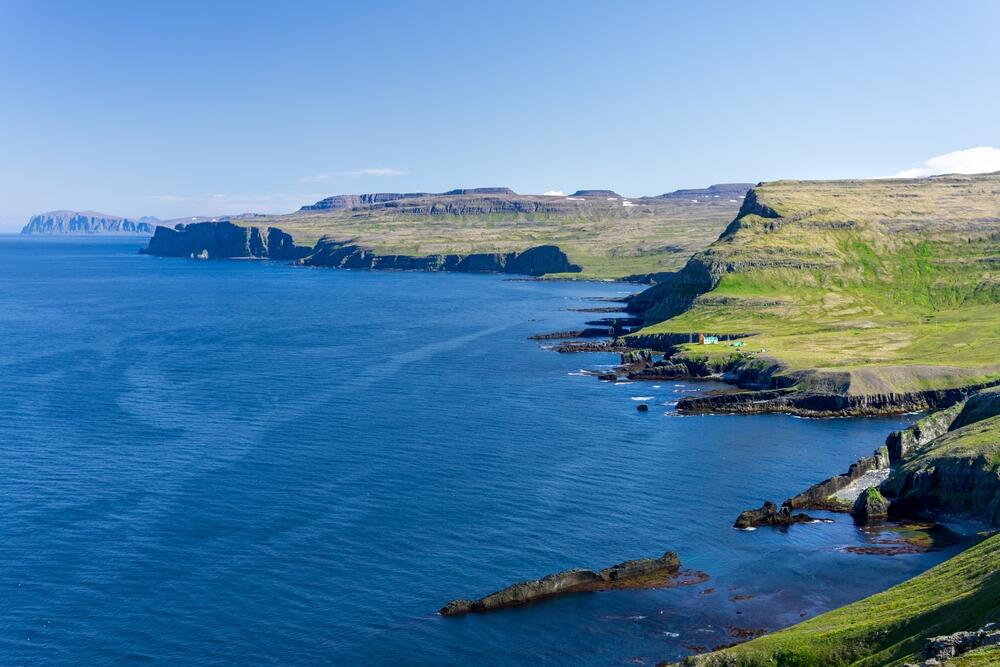 Vue panoramique sur les falaises verdoyantes de Hornstrandir surplombant l'océan, avec des montagnes en arrière-plan et des côtes déchiquetées.