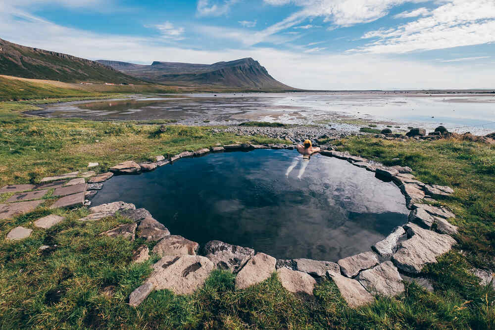 Une personne profitant d'une petite source chaude en plein air avec vue sur la mer et les montagnes environnantes.