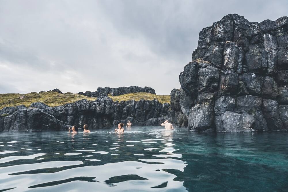 Un groupe de personnes se baignant dans une piscine naturelle entourée de formations rocheuses volcaniques sombres.