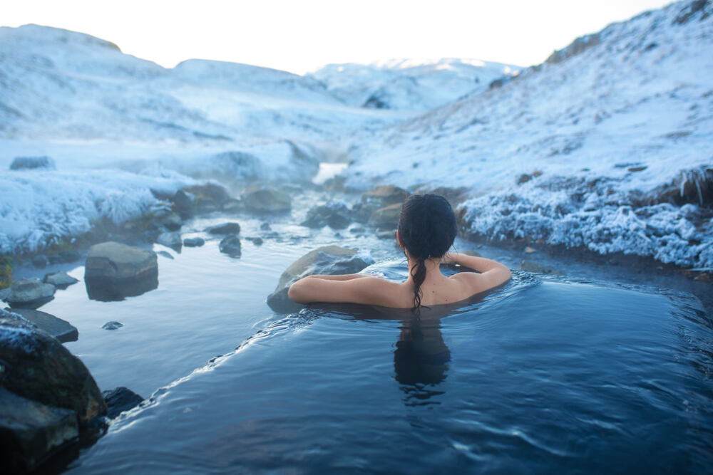 Une femme se relaxant dans une source chaude en plein hiver, entourée de paysages enneigés et de ruisseaux gelés.