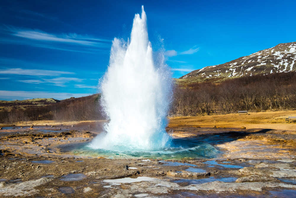 Un geyser éclatant dans les airs avec une puissante colonne d'eau sous un ciel bleu clair.