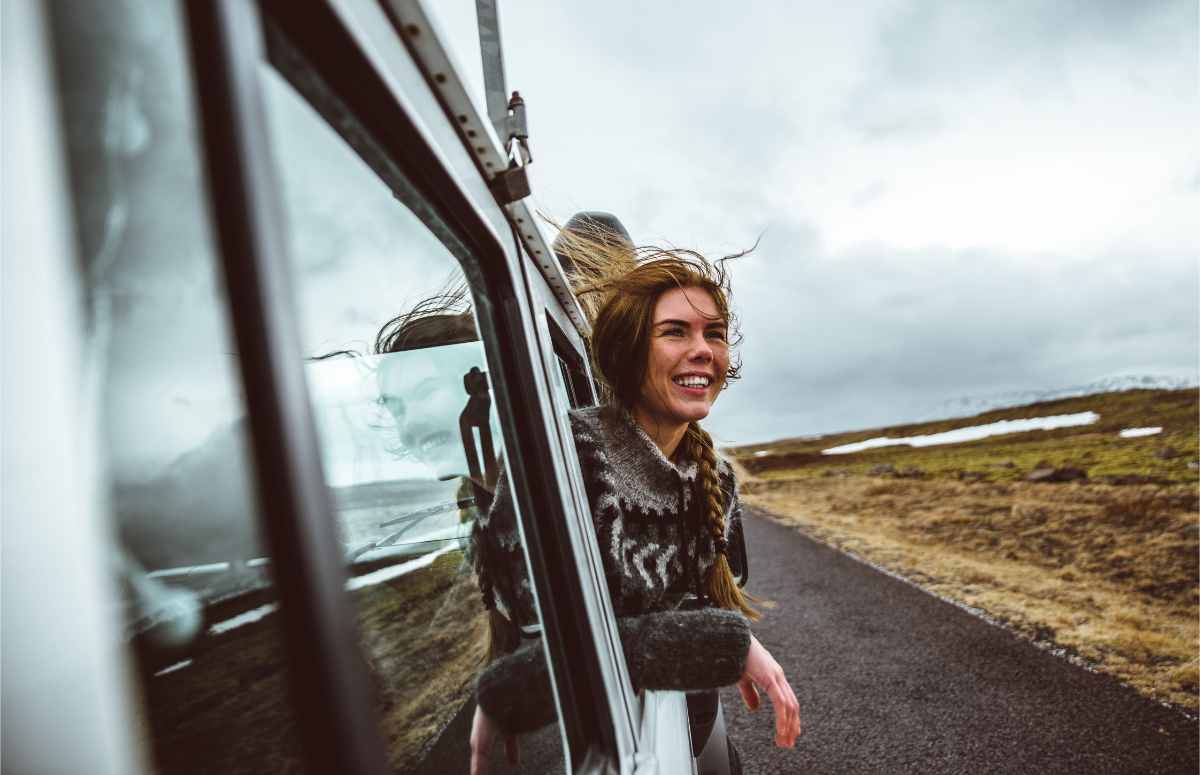 Femme sortant la tête de son véhicule de location avec un air heureux