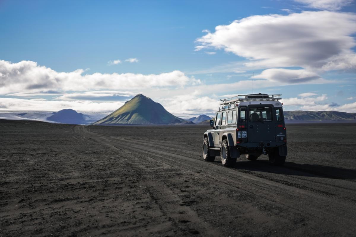 Jeep traversant un paysage volcanique avec une impressionnante montagne conique à l'arrière.