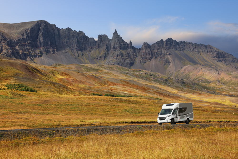 Camping-car roulant à travers les paysages colorés et montagneux d’Islande sous un ciel bleu clair.