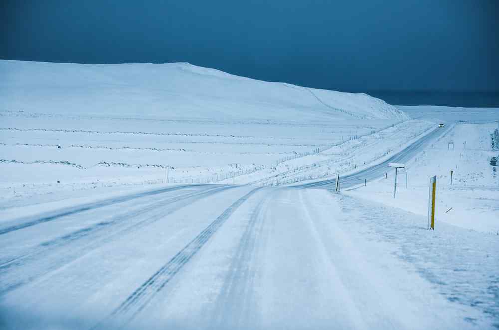 Route rurale verglacée traversant un paysage islandais enneigé sous un ciel sombre.