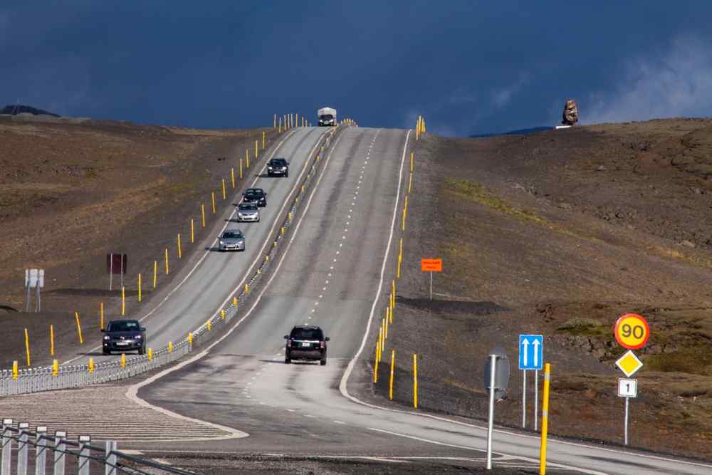 Voitures circulant sur la Route 1 en Islande près d’un panneau de limitation de vitesse à 90 km/h dans un paysage volcanique isolé.